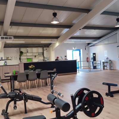 Fitnessbereich mit Geräten sowie Sitzbereich und Empfang im Hintergrund.