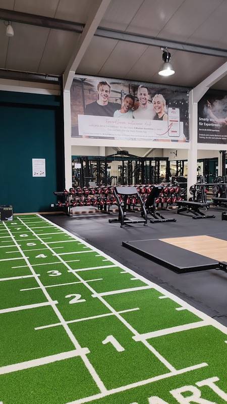 Moderner Fitnessbereich mit Kunstrasen-Laufbahn, Hantelbereich und Trainingsgeräten