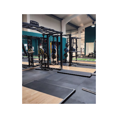 Freihantelbereich im Fitnessstudio mit Racks, Langhanteln und Trainingsmatten im Vordergrund.